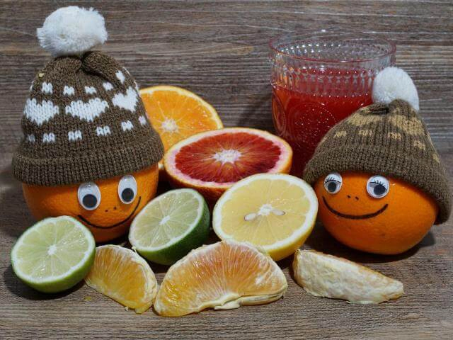 nell'immagine, il primo piano di diverse varietà di agrumi sia interi che a fette. In primo piano due arance a cui sono stati applicati occhi, naso e bocca e un cappellino di lana,