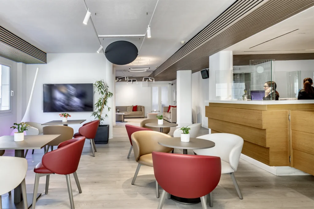 Nell'immagine, la Reception dell'Hotel Residence Italia: si vede il bancone sulla destra con una ragazza dello staff impegnata in una telefonata. Sulla sinistra ci sono invece alcuni tavolini con delle poltroncine. Alla parete, è appesa una TV.