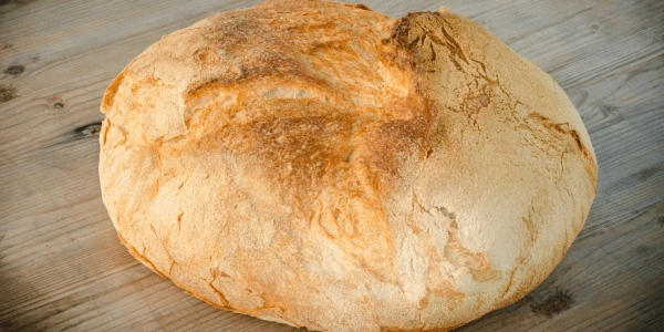 Nell'immagine, il primo piano di una pagnotta di pane poggiata su un tavolo di legno.