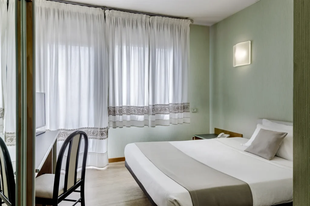 Nell'immagine, la camera singola Superior dell'Hotel Residence Italia: si vede il letto alla francese e, di fronte, un tavolo su cui è poggiata la TV. Ci sono anche delle finestre con le tende tirate.